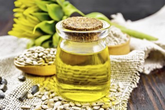 Sunflower oil in glass jar, spoon with peeled seeds and flour in bowl on burlap, a flower on wooden