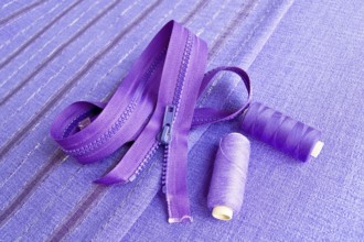 Locking zipper and two reels of thread on the purple plain and striped fabrics