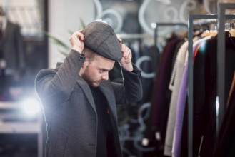 Individual trying on a flat cap in a fashionable clothing store setting