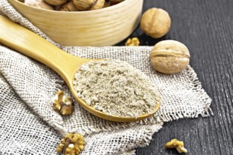 Walnut flour in a spoon on burlap, nuts on a table and in a bowl against dark wooden board