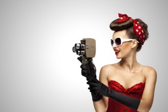 Retro photo of a pin up girl with an old 8 mm camera on a grey background