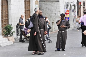 Group of monks in traditional robes on a busy city street, Assisi, Umbria, Italy