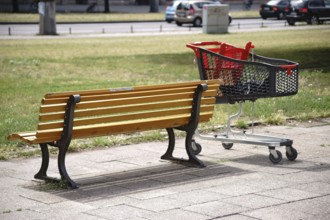 A modern plastic shopping trolley stands next to a park bench in the city