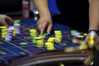 Roulette table with human hands putting down chips in casino. Roulette wheel in the foreground.