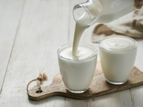 Pouring homemade kefir, buttermilk or yogurt with probiotics. Yogurt flowing from glass bottle on