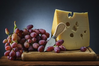 Piece of cheese and grape with knife on wooden chopping board black gradient background
