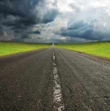 Old broken asphault road in green field over blue cloudy sky