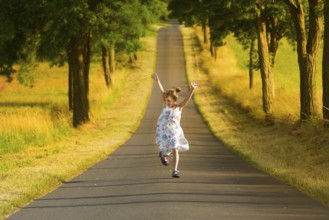 A little girl in a summer dress runs along a street in the light of a summer evening, jumping and