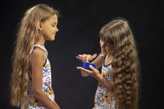 A girl puts jar cream on her finger, another girl sits nearby