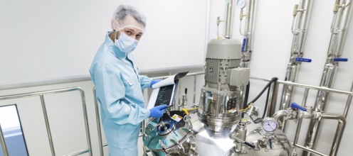 Widescreen picture, scientist in blue laboratory suit and gas mask stand in clean room and check