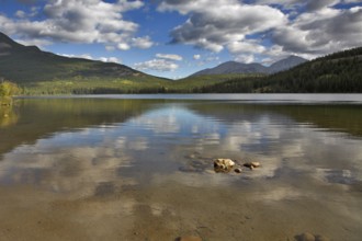 Clouds shining on the sun are reflected in northern lake surrounded by mountains