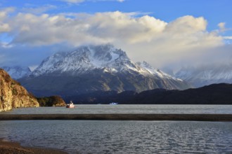 Gray lake and snow-capped mountains. By the banks of the red tourist ship sails. Summer sunset