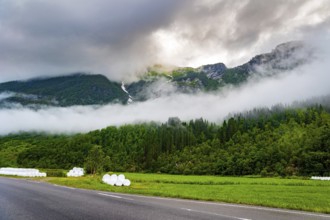 Wide asphalt road crosses the valley. Jostedalsbreen Park. Valley surrounded by high forested