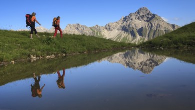Two female mountaineers are reflected in a lake by the majestic Biberkopf in the background, Allgäu