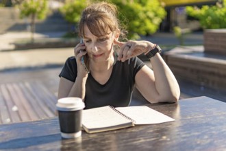 Woman over 50 reviewing notes while on a call with coffee outdoors