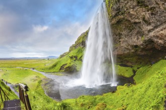Seljalandsfoss waterfall in July. Large rainbow decorates a drop of water. The warm July day in