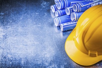 Blue engineering drawings yellow hard hat on scratched metallic background construction concept