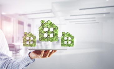 Close of businessman holding tablet pc with house sign made of connected gears. Mixed media
