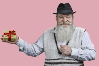 Portrait of aged man with gift box. Isolated on pink