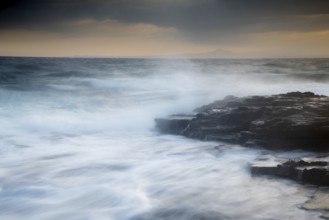 Rocky seashore with wavy ocean and waves crashing on the rocks. Long exposure photography
