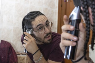 Guy in towel cutting his hair in front of mirror at home. Health Care Concept.