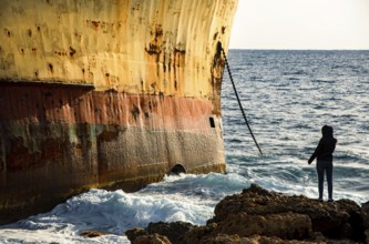 Person looking at moored shipwreck on a rocky coast line and wind waves. Paphos Cyprus