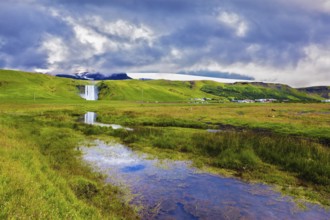 Huge full-flowing waterfall Skogafoss reflected in small creek. Spectacular reflection