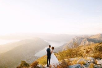 The bride and groom stand on the top of Mount Lovcen overlooking the Bay of Kotor, smile and hug