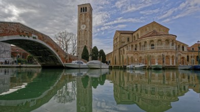 Scenic canal with boats reflecting a historic church and tall bell tower under a cloudy sky, Ponte
