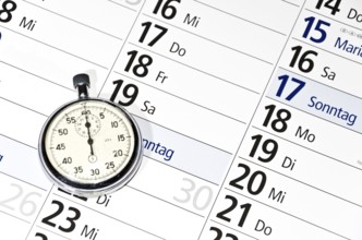Stopwatch lying on calendar (with captions of the days of the week in German)