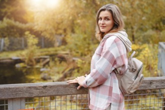 Portrait of cute young woman in casual wear in autumn, standing on bridge against background of an