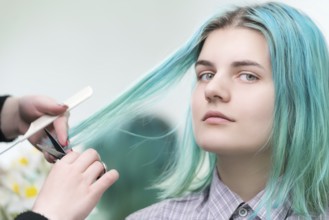 Hairdresser cutting with scissors long green hair of young woman. Hair care in professional beauty