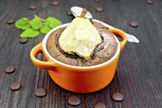 Cake with chocolate and pear in red roaster, mint and spoon on a background of dark wood planks