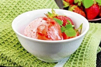 Ice cream strawberry in a white bowl with berries and syrup on a green napkin on a background of a