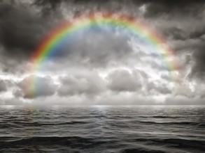 A dark sky background with a colorful rainbow at the ocean