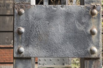 Close-up of a weathered gray metal plate attached to a larger metal structure with rivets, showing