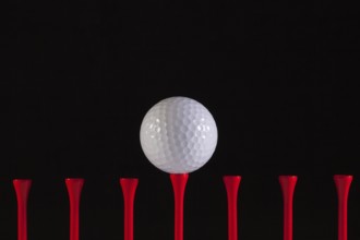 Golf ball and red tee on a black background