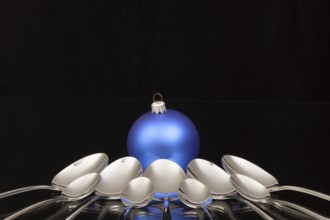 Blue Christmas decoration and nine spoons on a black glass desk