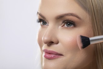 This is a professional makeup application showcasing a model skillfully utilizing a blush brush for