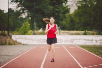 Beautiful young athlete Caucasian woman with big breasts in red T-shirt and short shorts running