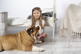 A young girl in a bedroom, sitting on the floor with her dog and stroking him. Child and dog. The