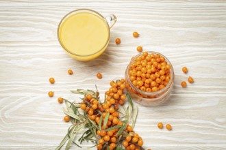 Sea buckthorn healthy hot tea in transparent glass cup, ripe berries in glass jar and branches with
