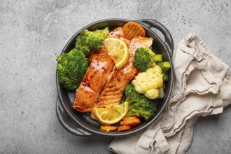 Healthy baked fish salmon steaks, broccoli, cauliflower, carrot in black cast iron casserole bowl