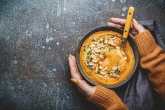 Female hands in yellow knitted sweater holding a bowl with pumpkin cream soup on dark stone