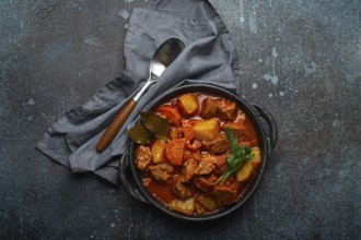 Beef meat stew with potatoes, carrot and delicious gravy in black casserole pot with bay leaves and