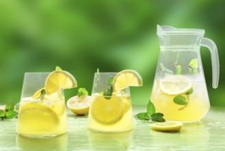 Lemonade with mint on a green background. Lemon water drink with ice. Two glasses and a pitcher.