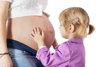 Daughter hugging mother's pregnant belly isolated on white