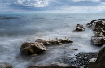 Seawaves splashing onto the sandy coast with pebbles and blue cloudy sky. Melanda coast, Pissouri