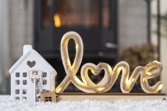 Key to house with keychain against background of fireplace stove with fire and firewood in