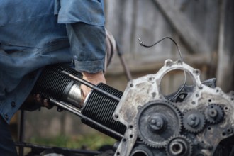 A person working on an engine outdoors, focusing on metal and mechanical components